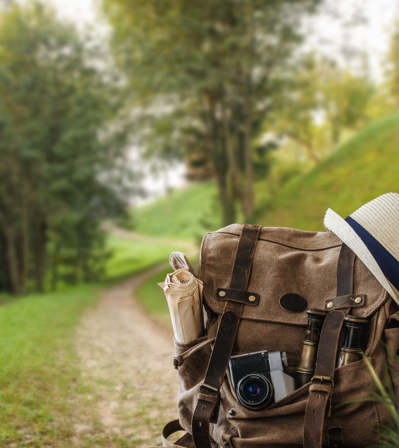 backpack with travel items sitting on gravel path through woods